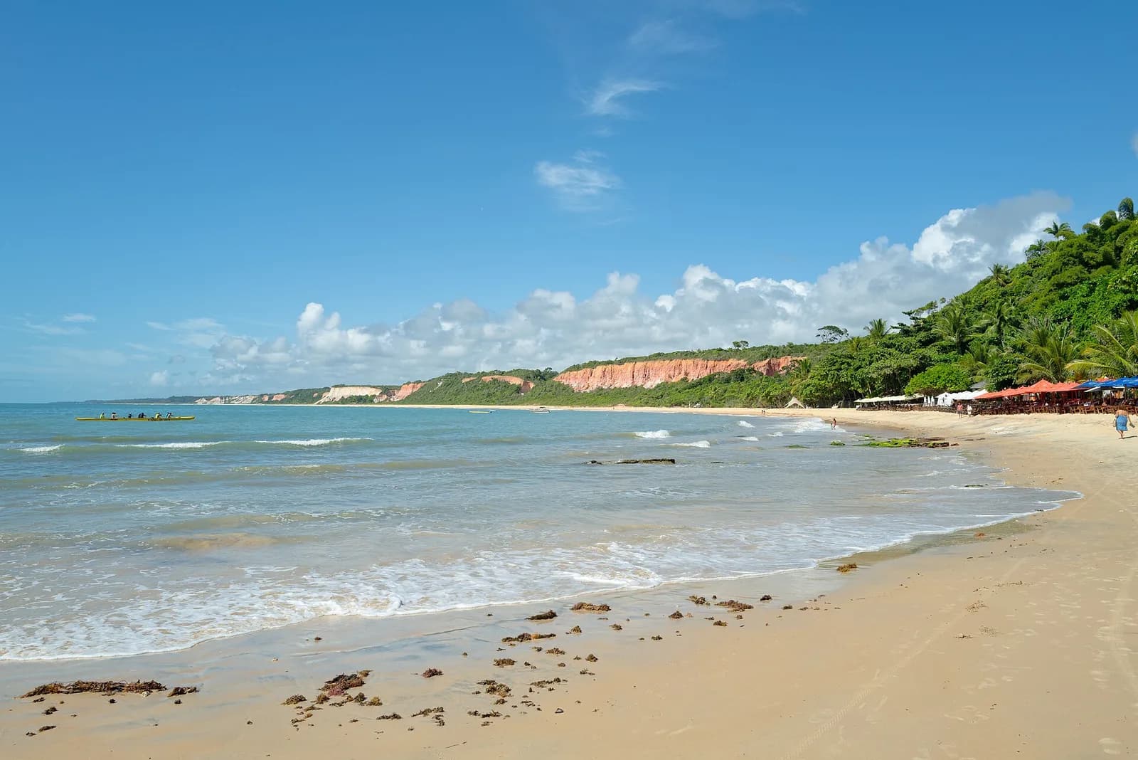 Praia de Arraial d'Ajuda com as falésias avermelhadas ao fundo e vegetação nativa na orla